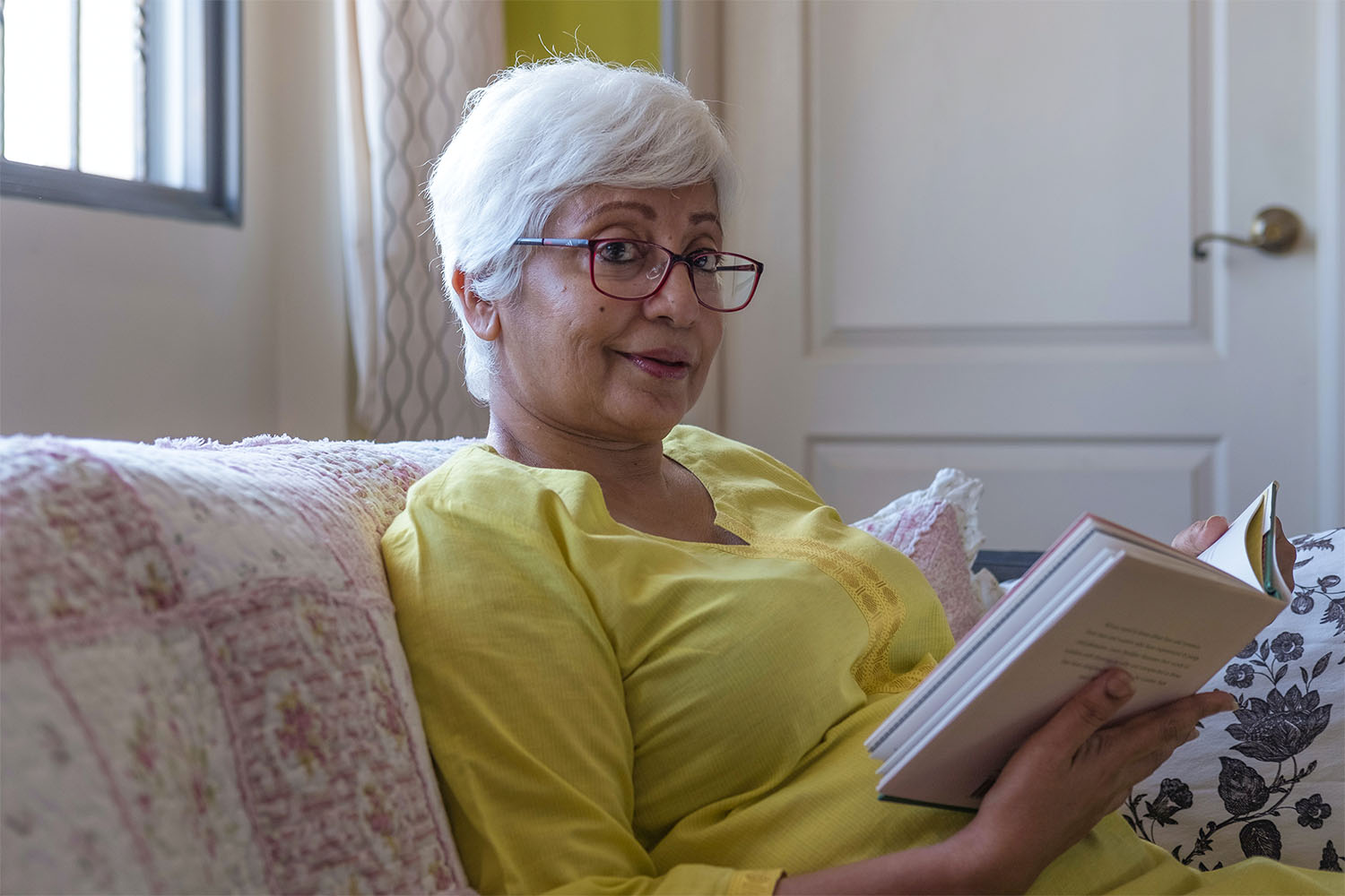 Lady wearing yellow shirt reading a book on a sofa